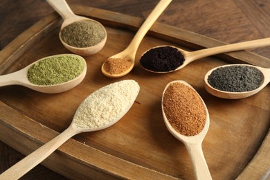 Different superfood powders in spoons on wooden table, closeup