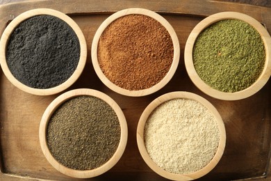 Different superfood powders in bowls on wooden board, top view