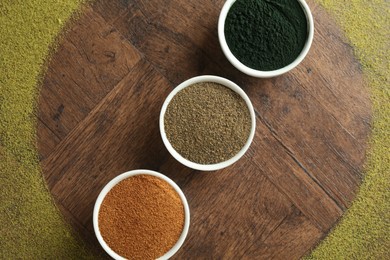 Photo of Different superfood powders in bowls on wooden table, flat lay