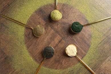 Different superfood powders in spoons on wooden table, flat lay