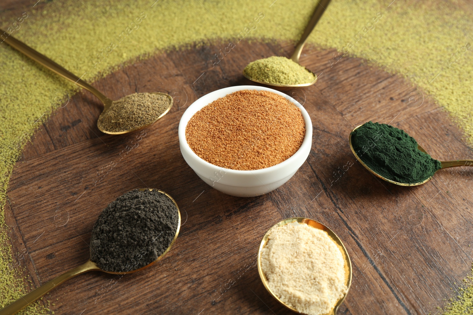 Photo of Different superfood powders in spoons and bowls on wooden table