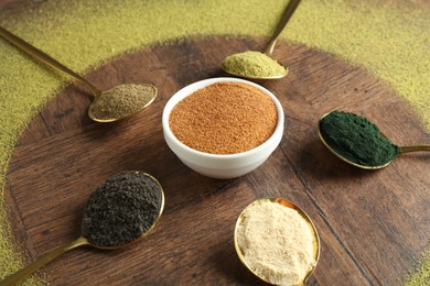 Photo of Different superfood powders in spoons and bowls on wooden table