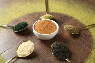 Photo of Different superfood powders in spoons and bowls on wooden table