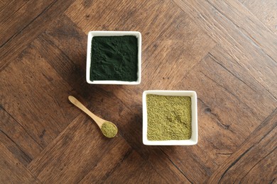 Different superfood powders in bowls and spoon on wooden table, top view