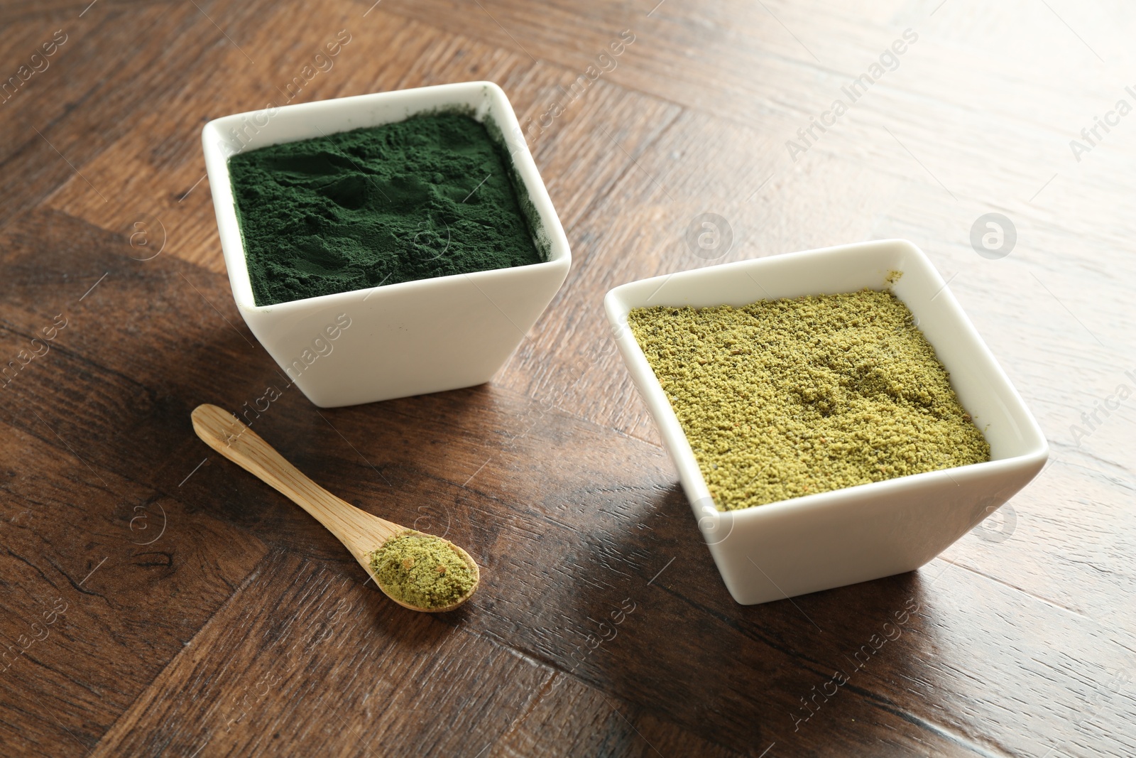 Photo of Different superfood powders in bowls and spoon on wooden table, closeup