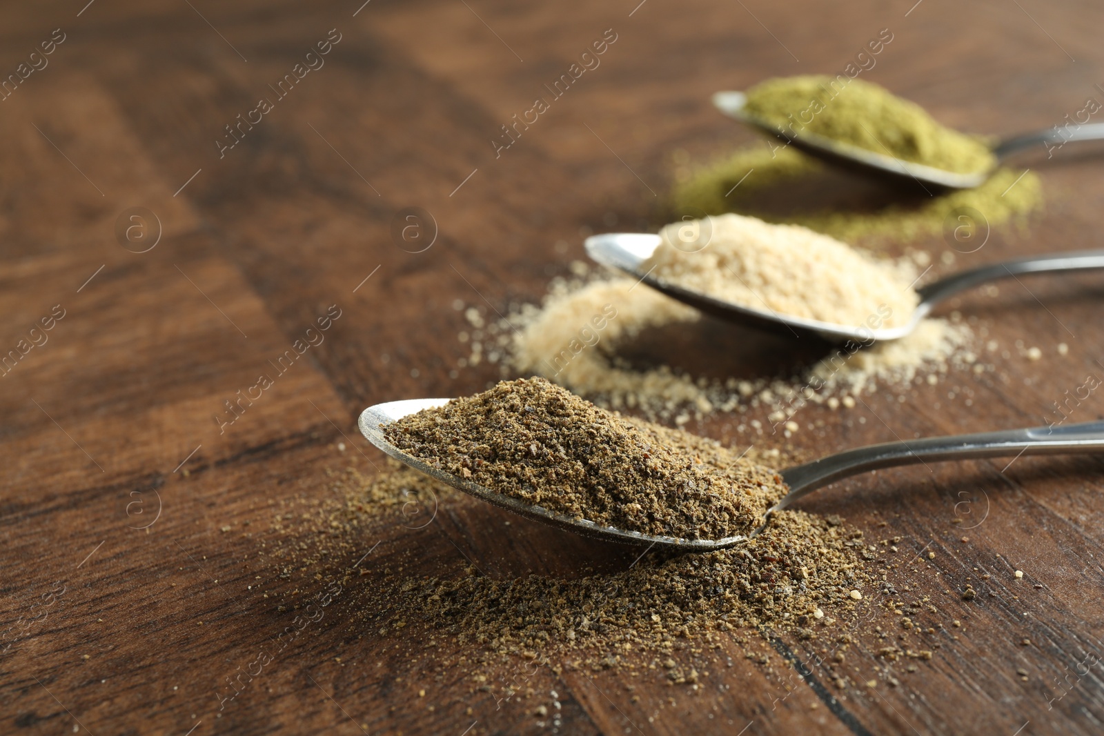 Photo of Different superfood powders in spoons on wooden table, closeup