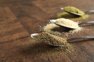 Different superfood powders in spoons on wooden table, closeup