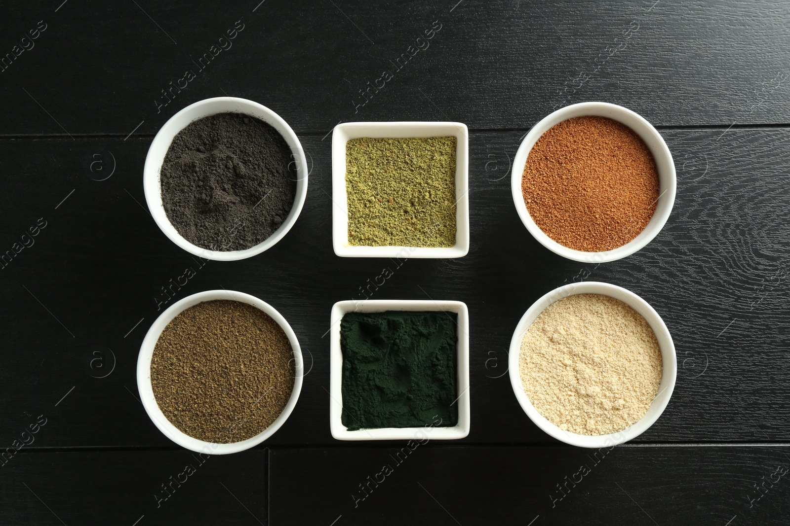 Photo of Different superfood powders in bowls on black wooden table, flat lay