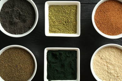 Different superfood powders in bowls on black wooden table, flat lay