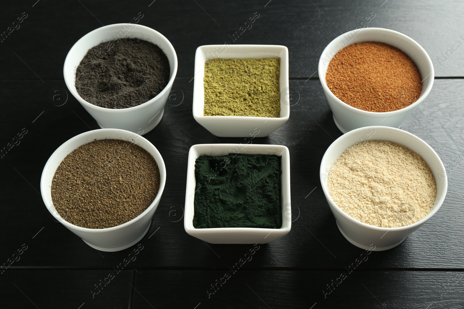 Photo of Different superfood powders in bowls on black wooden table