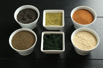 Photo of Different superfood powders in bowls on black wooden table