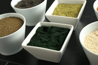 Different superfood powders in bowls on black wooden table, closeup