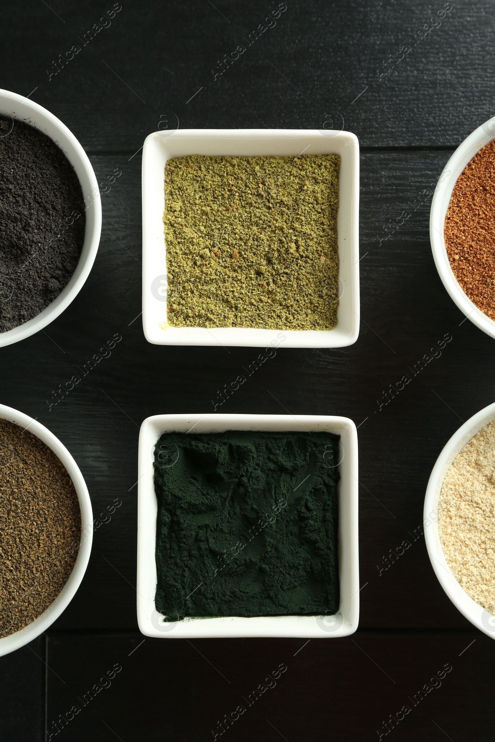 Photo of Different superfood powders in bowls on black wooden table, flat lay