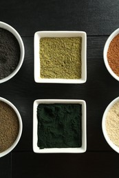 Photo of Different superfood powders in bowls on black wooden table, flat lay