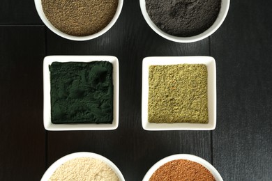 Different superfood powders in bowls on black wooden table, flat lay