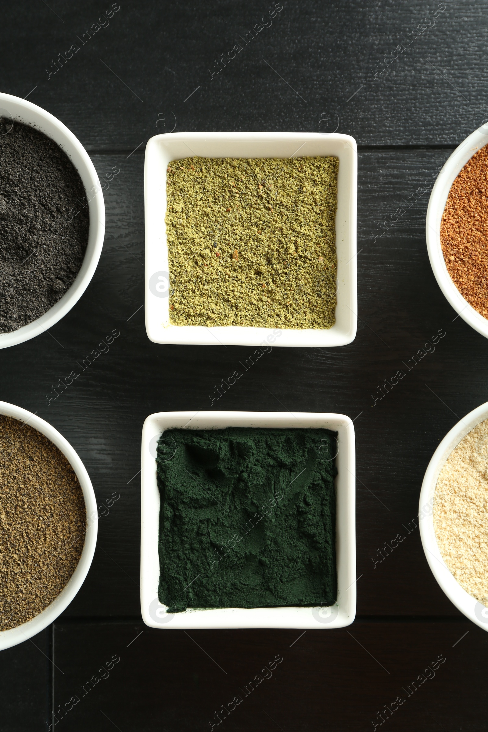 Photo of Different superfood powders in bowls on black wooden table, flat lay