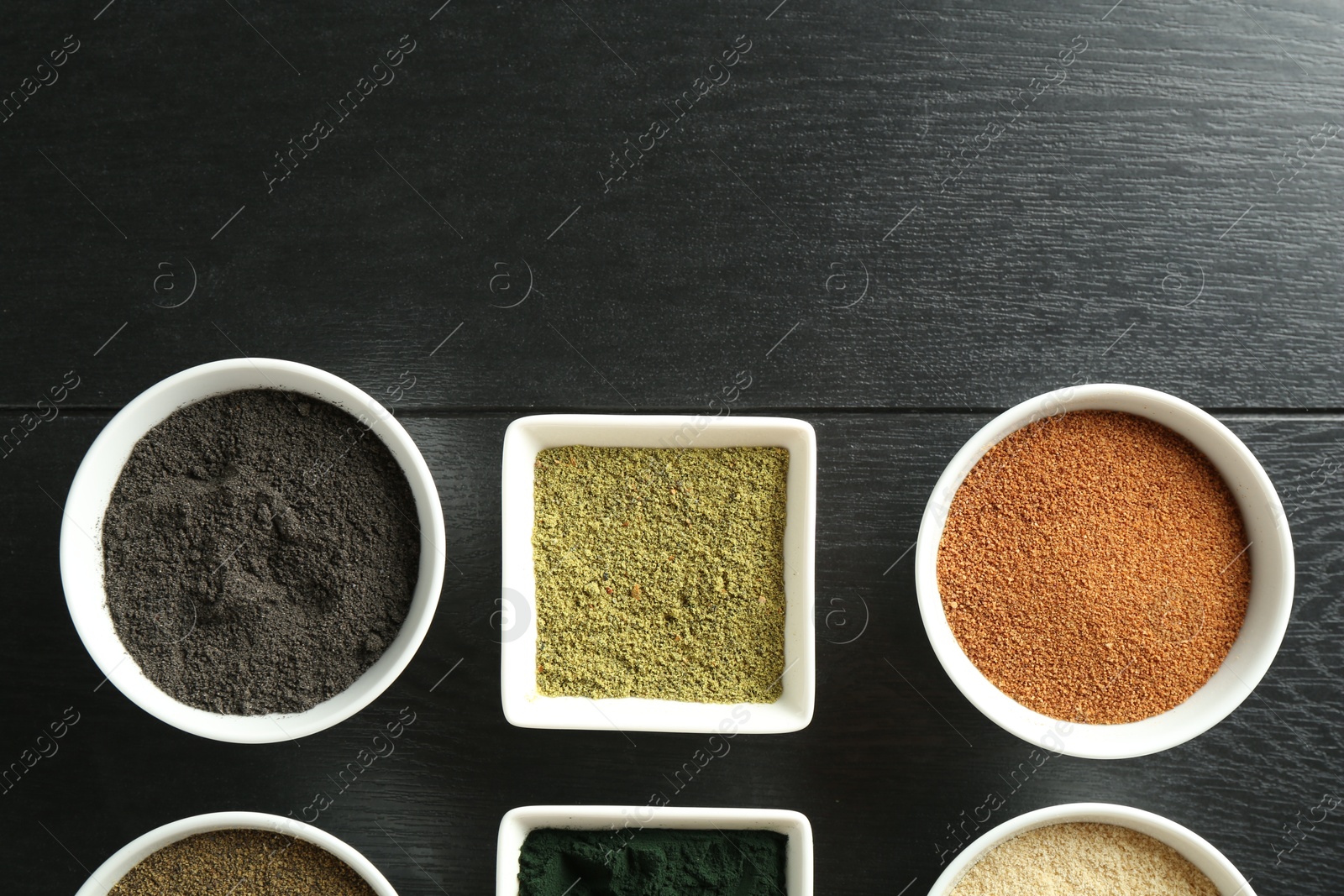 Photo of Different superfood powders in bowls on black wooden table, flat lay