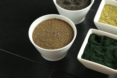 Photo of Different superfood powders in bowls on black wooden table, closeup