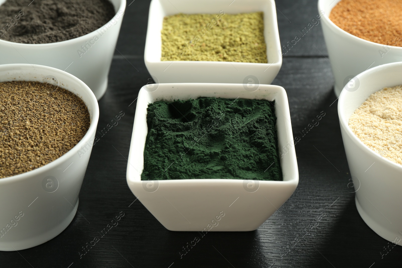 Photo of Different superfood powders in bowls on black wooden table, closeup