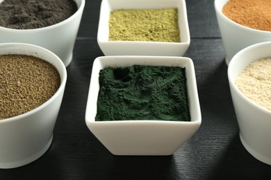 Photo of Different superfood powders in bowls on black wooden table, closeup