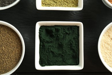 Photo of Different superfood powders in bowls on black wooden table, flat lay