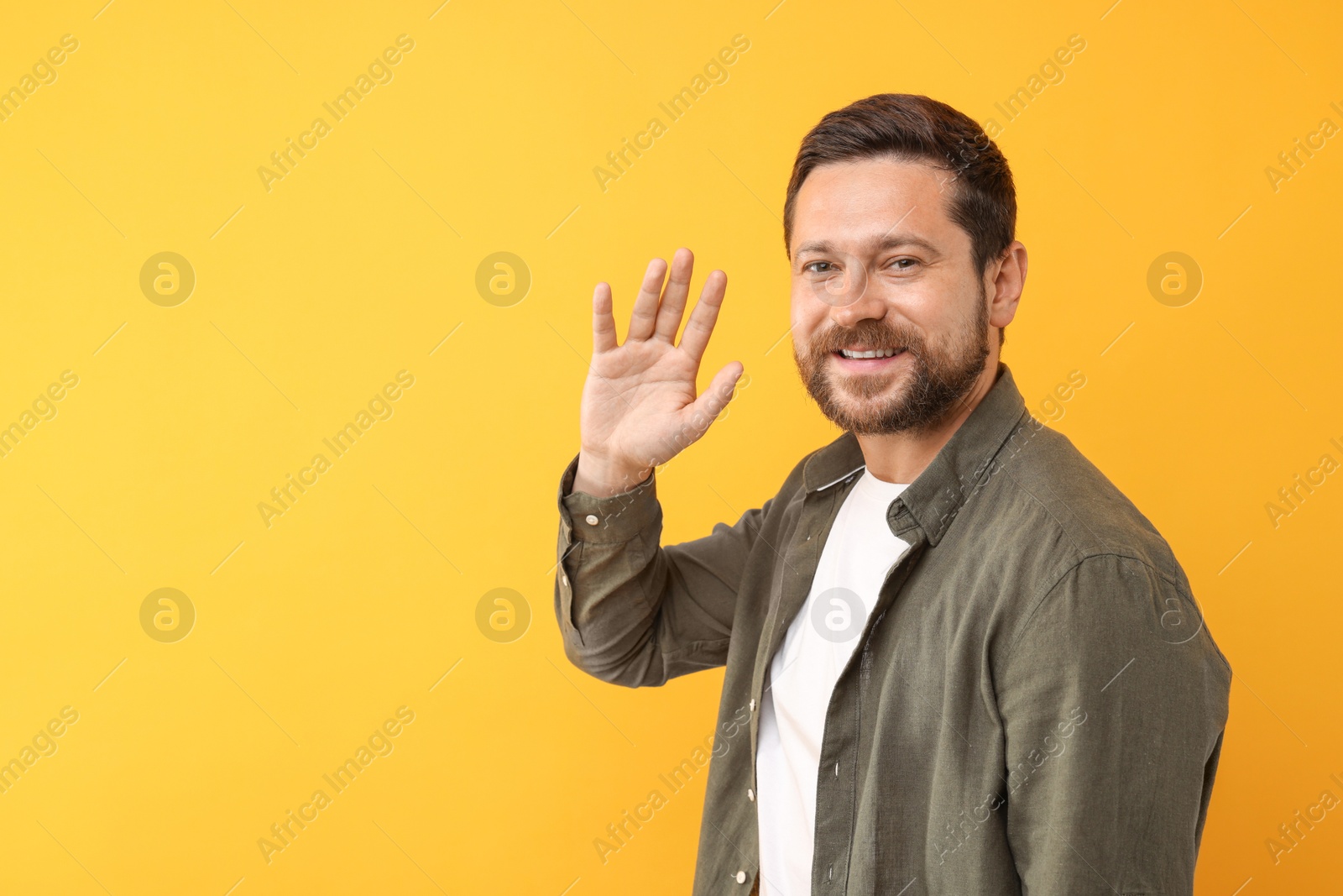 Photo of Cheerful man waving on orange background. Space for text