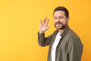 Cheerful man waving on orange background. Space for text