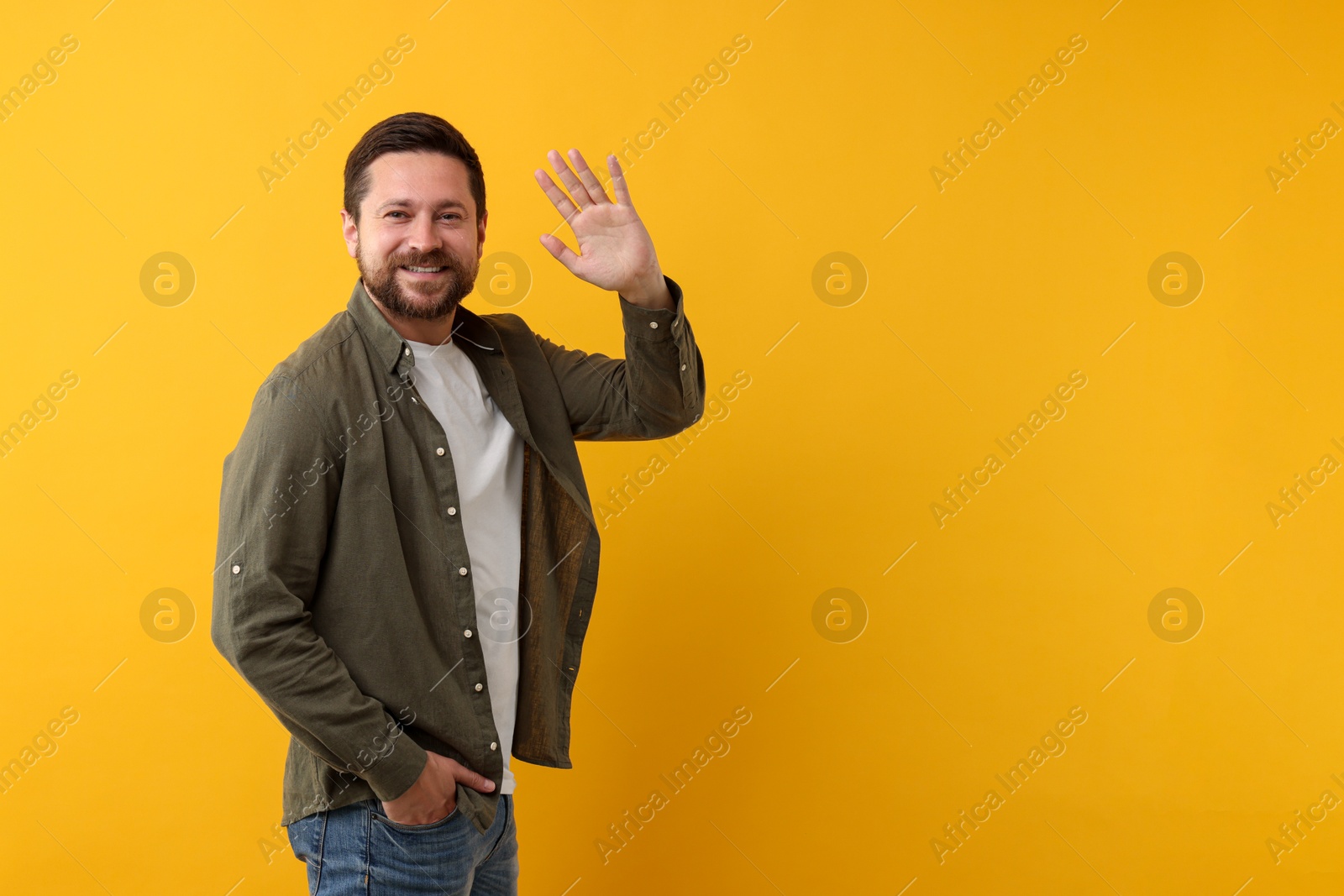 Photo of Cheerful man waving on orange background. Space for text