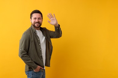 Cheerful man waving on orange background. Space for text