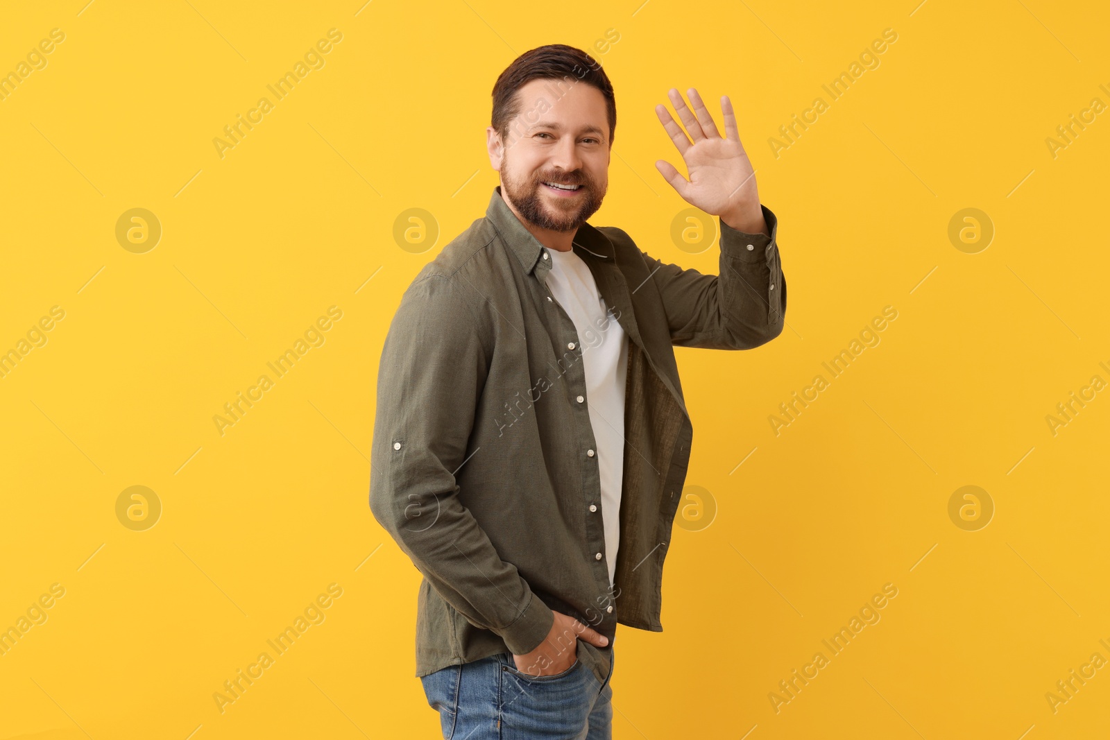 Photo of Cheerful handsome man waving on orange background