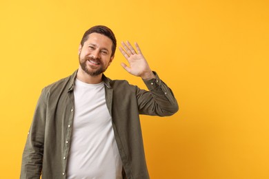 Photo of Cheerful man waving on orange background. Space for text