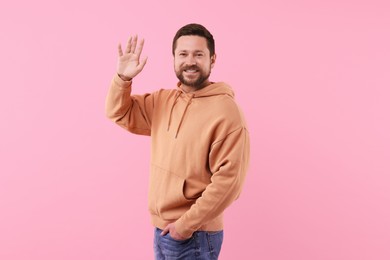 Cheerful handsome man waving on pink background