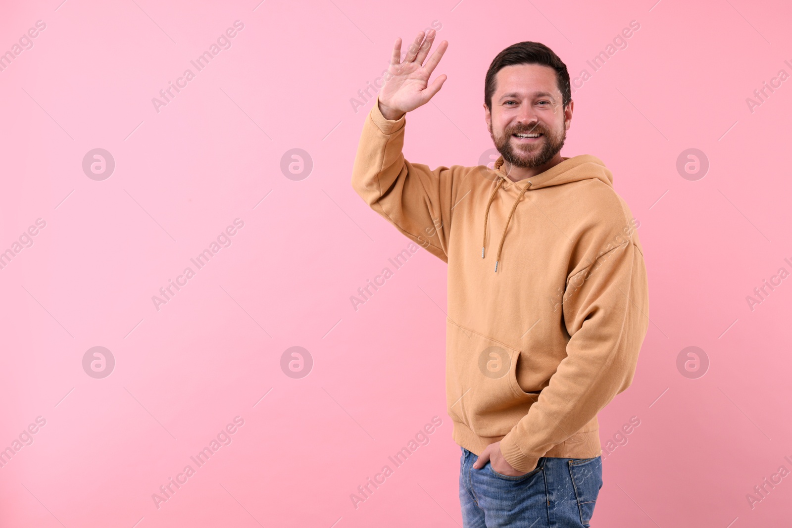 Photo of Cheerful man waving on pink background. Space for text