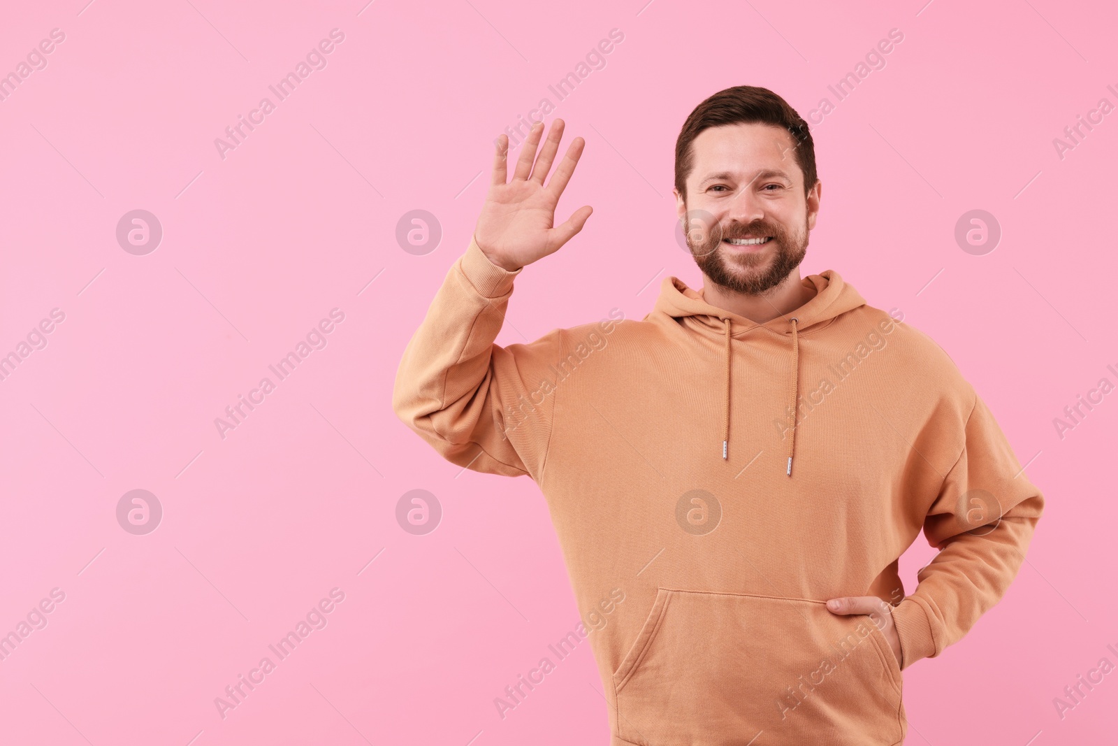 Photo of Cheerful man waving on pink background. Space for text