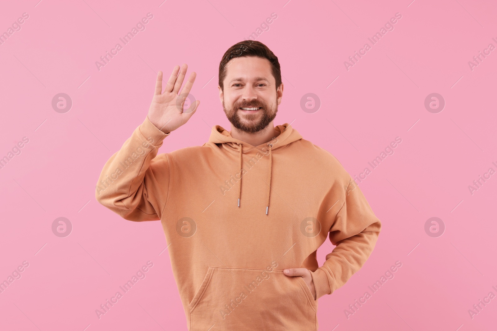 Photo of Cheerful handsome man waving on pink background