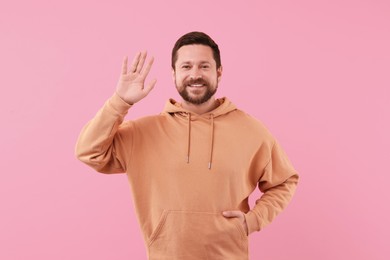 Cheerful handsome man waving on pink background