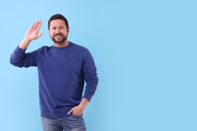 Cheerful man waving on light blue background. Space for text