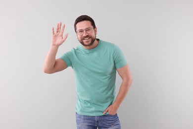 Photo of Cheerful handsome man waving on light background