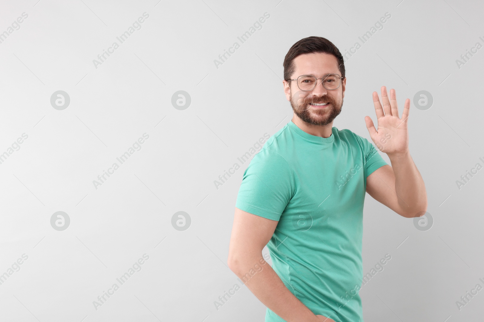 Photo of Cheerful man waving on light background. Space for text