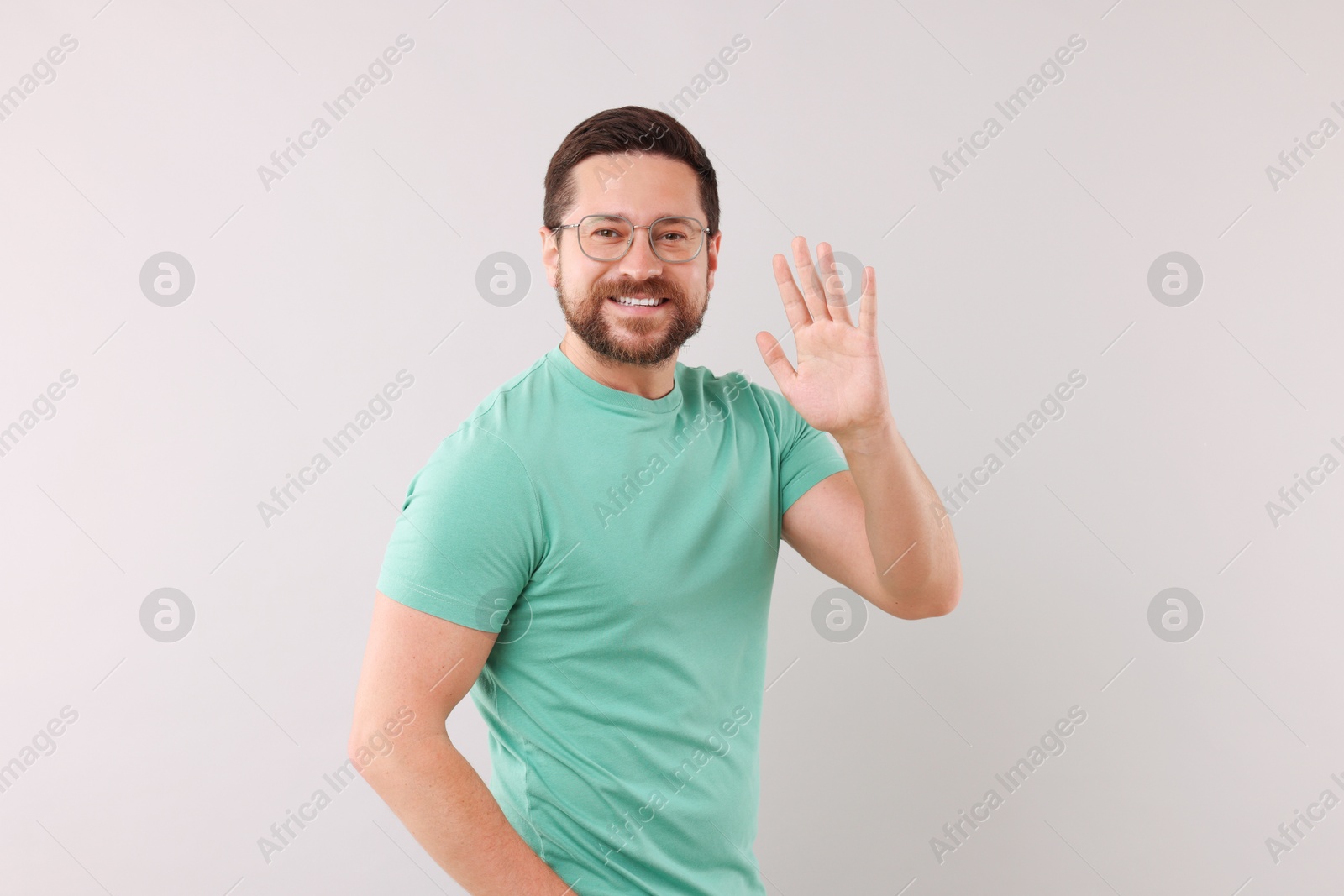 Photo of Cheerful handsome man waving on light background