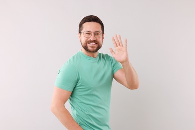 Cheerful handsome man waving on light background