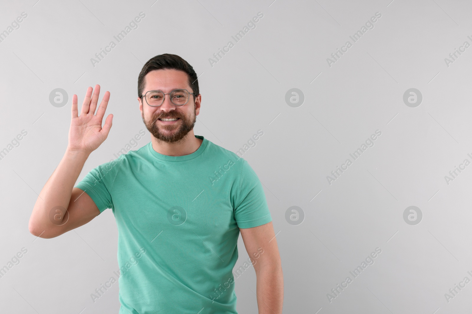 Photo of Cheerful man waving on light background. Space for text