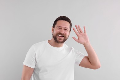 Cheerful handsome man waving on light background