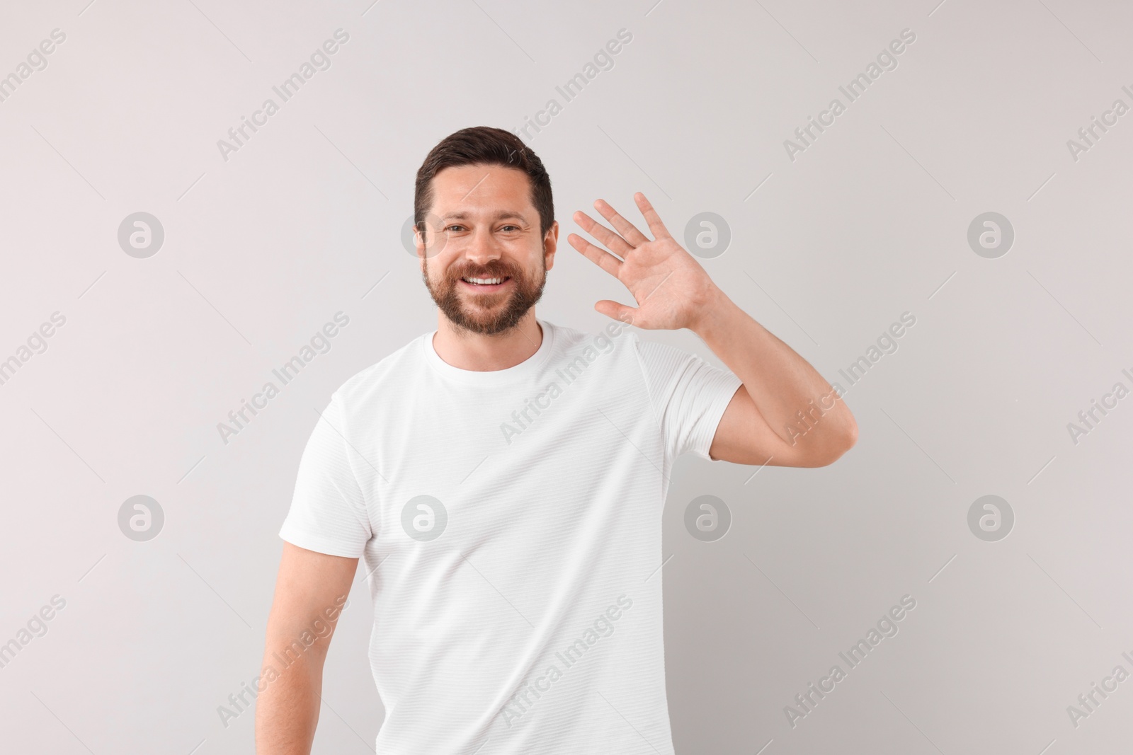 Photo of Cheerful handsome man waving on light background