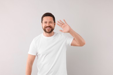 Cheerful handsome man waving on light background