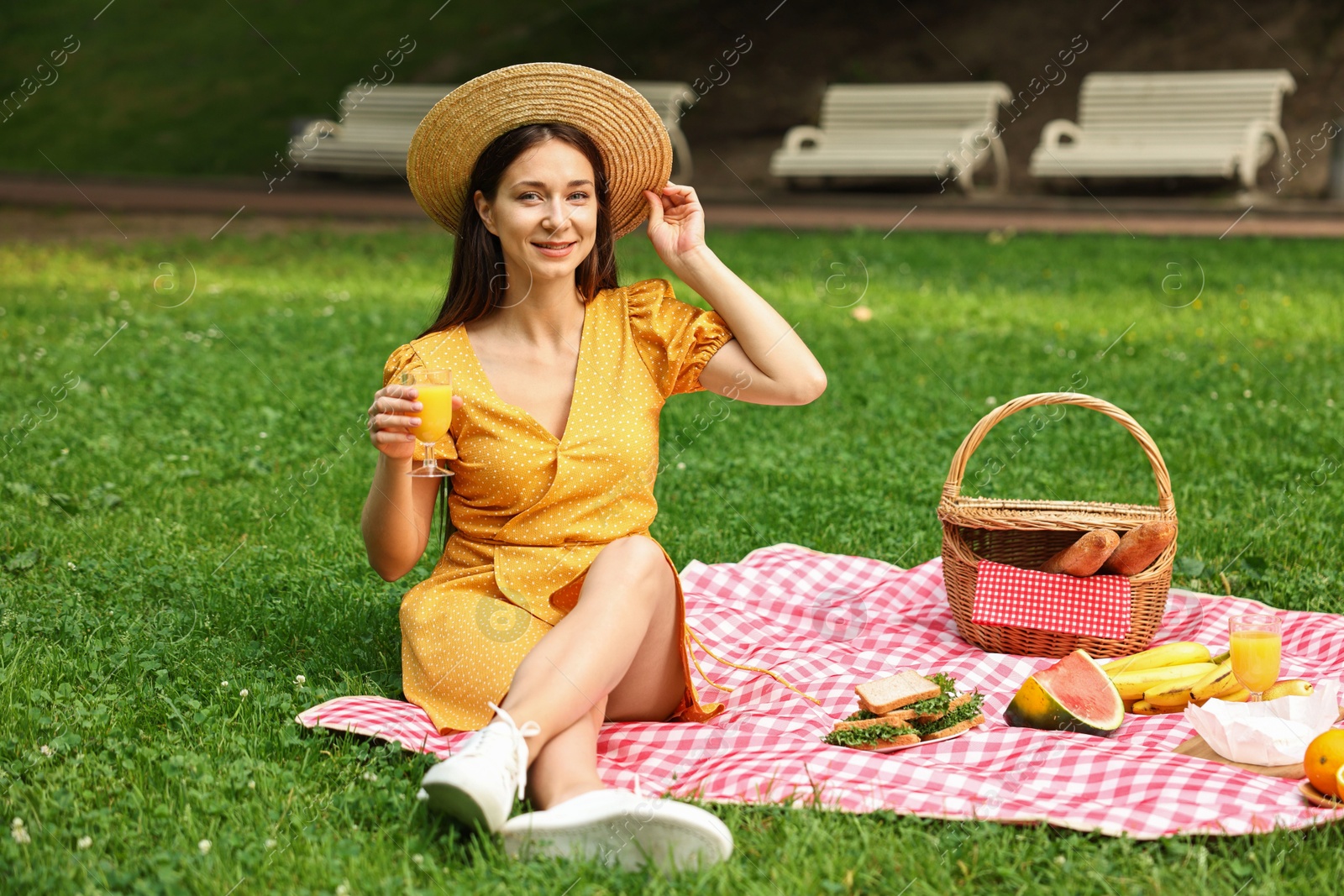 Photo of Smiling woman with glass of juice having picnic on green grass