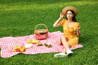 Beautiful woman with glass of juice having picnic on green grass