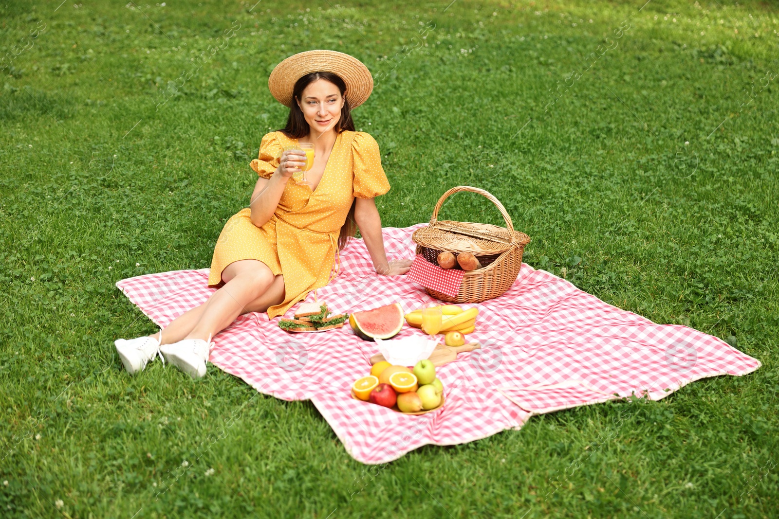 Photo of Beautiful woman with glass of juice having picnic on green grass