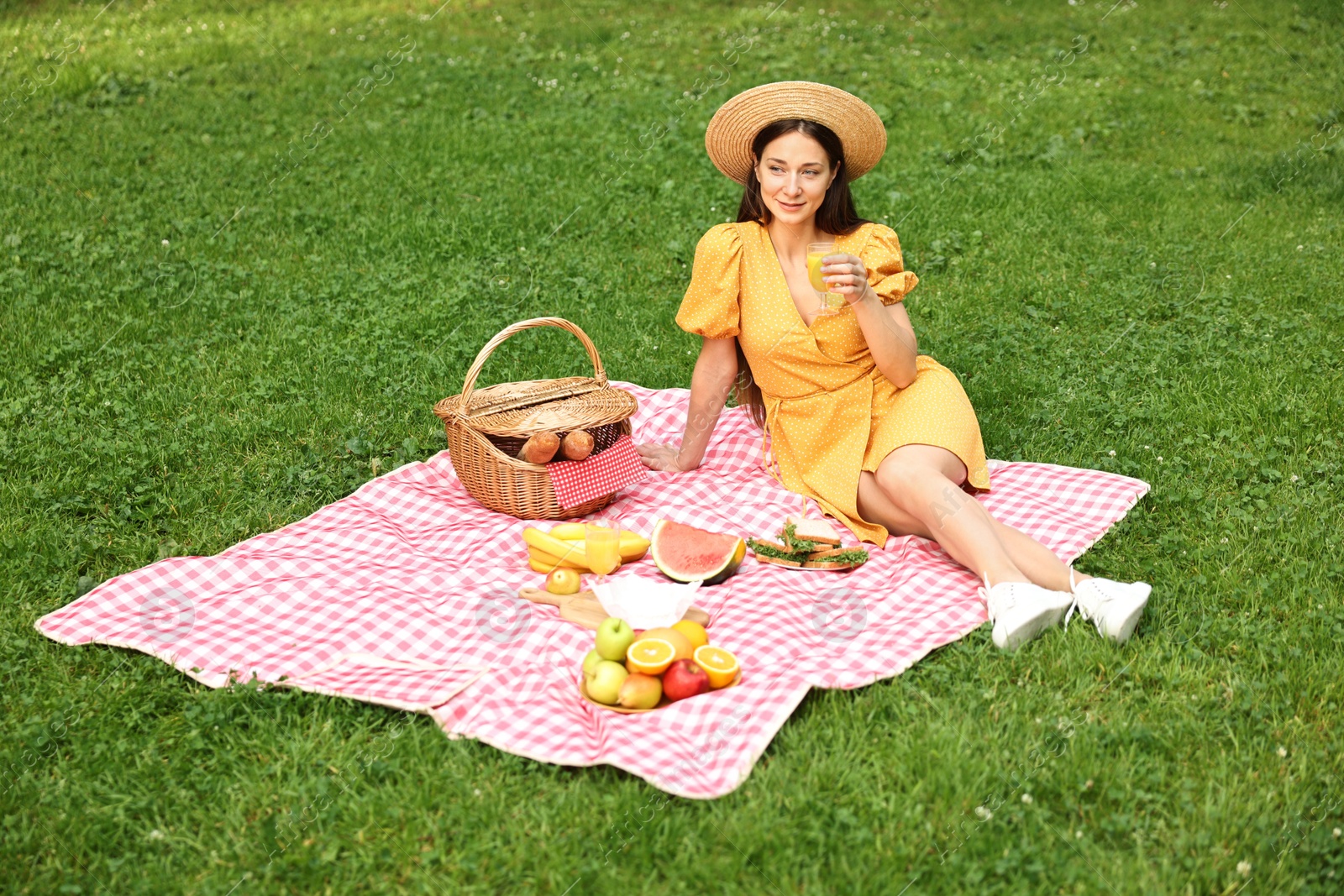 Photo of Beautiful woman with glass of juice having picnic on green grass