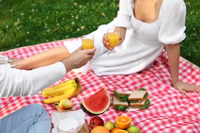 Photo of Lovely couple clinking glasses of juice on picnic blanket outdoors, closeup